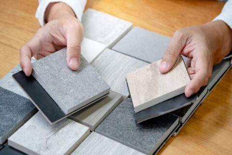 Hands holding stone countertop samples in various shades of gray and beige on a wooden table in Durango, CO