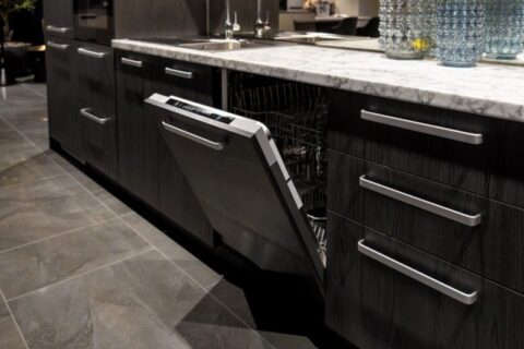 Modern kitchen with dark wood cabinets, marble countertop, built-in sink, and open dishwasher in Durango, CO